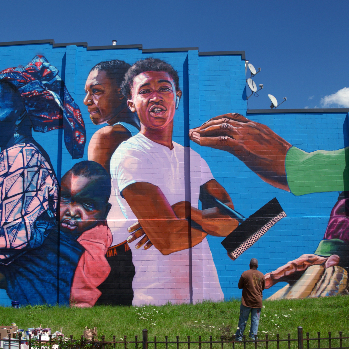 Part of the mural "African in America." Two Black women look to the left while two Black men look forward. The artist is standing in the grass looking at the mural.