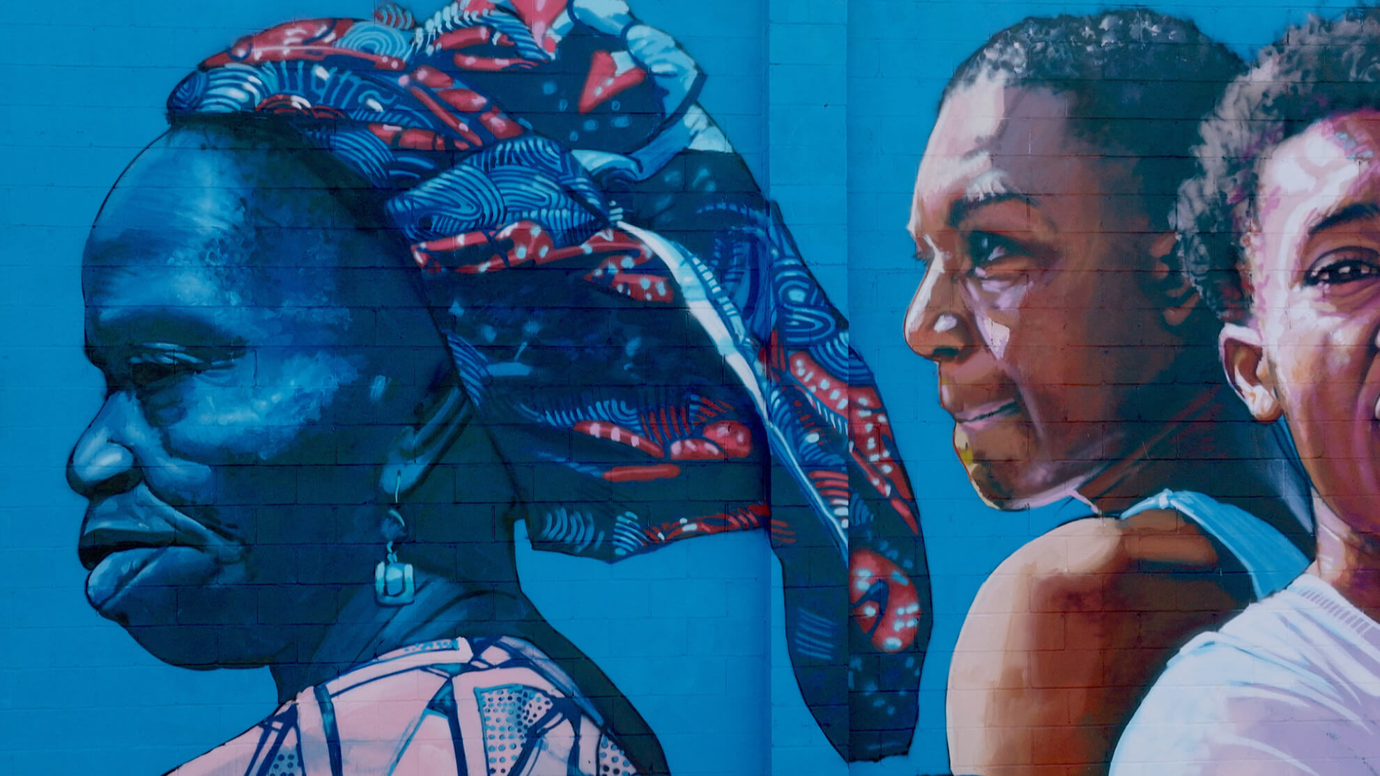 A close-up of the two women in the mural. The older woman on the left is rendered in more blue tones reminiscent of night while the younger woman on the right in bright tones resembling daylight.