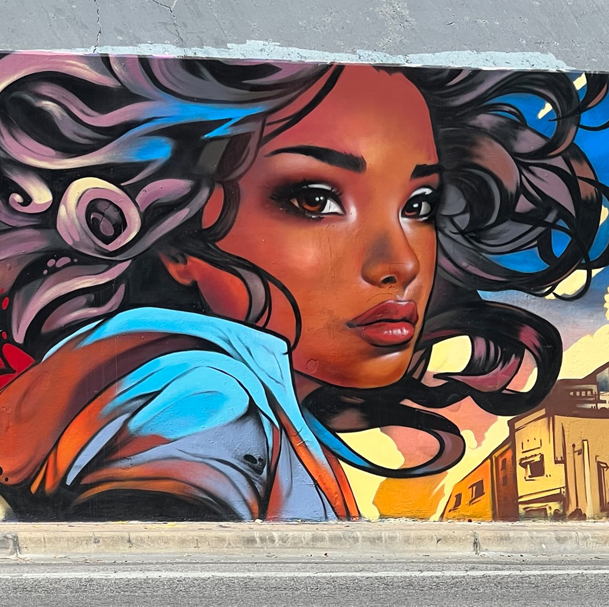 Part of the mural "Chase The Light." A Black woman is depicted with long, curly hair that fades into colorful artistic designs.