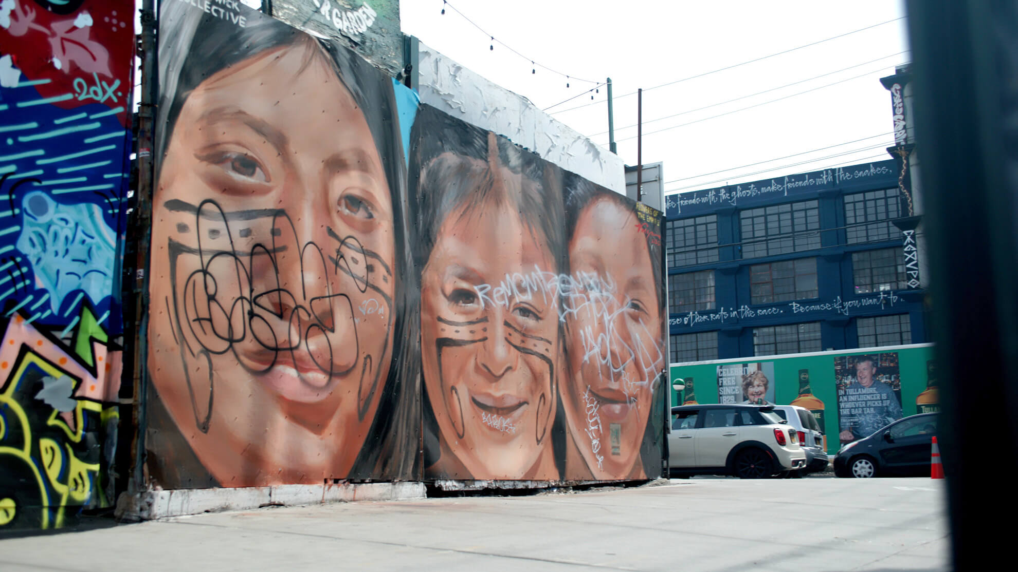 An angled shot of the mural before it was mended. Graffiti has been drawn over all of the faces, obscuring them.