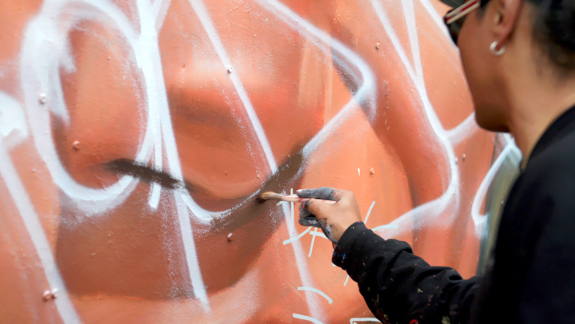 A close-up of the artist, Robert Vargas, seen from the side beginning to mend the mural using a brush.